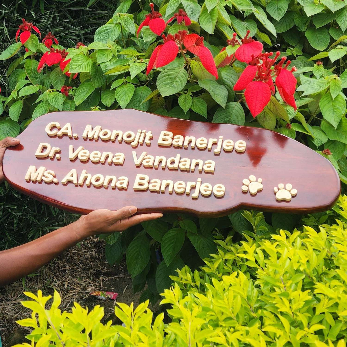 A custom wooden nameplate with raised 3d wood gold lettering reading 'CA. Monojit Banerjee, Dr. Veena Vandana' and pug marks for a pet 